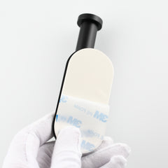 Black 304 stainless steel adhesive toilet paper holder with 3M backing, held in gloved hand.