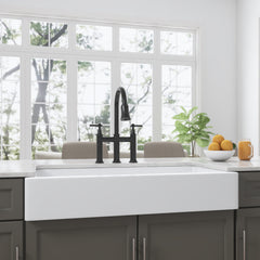White ceramic 36-inch apron-front farmhouse sink with black bridge faucet in a bright kitchen.