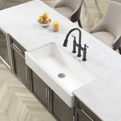 White 36-inch ceramic farmhouse apron front kitchen sink with black faucet on marble countertop.