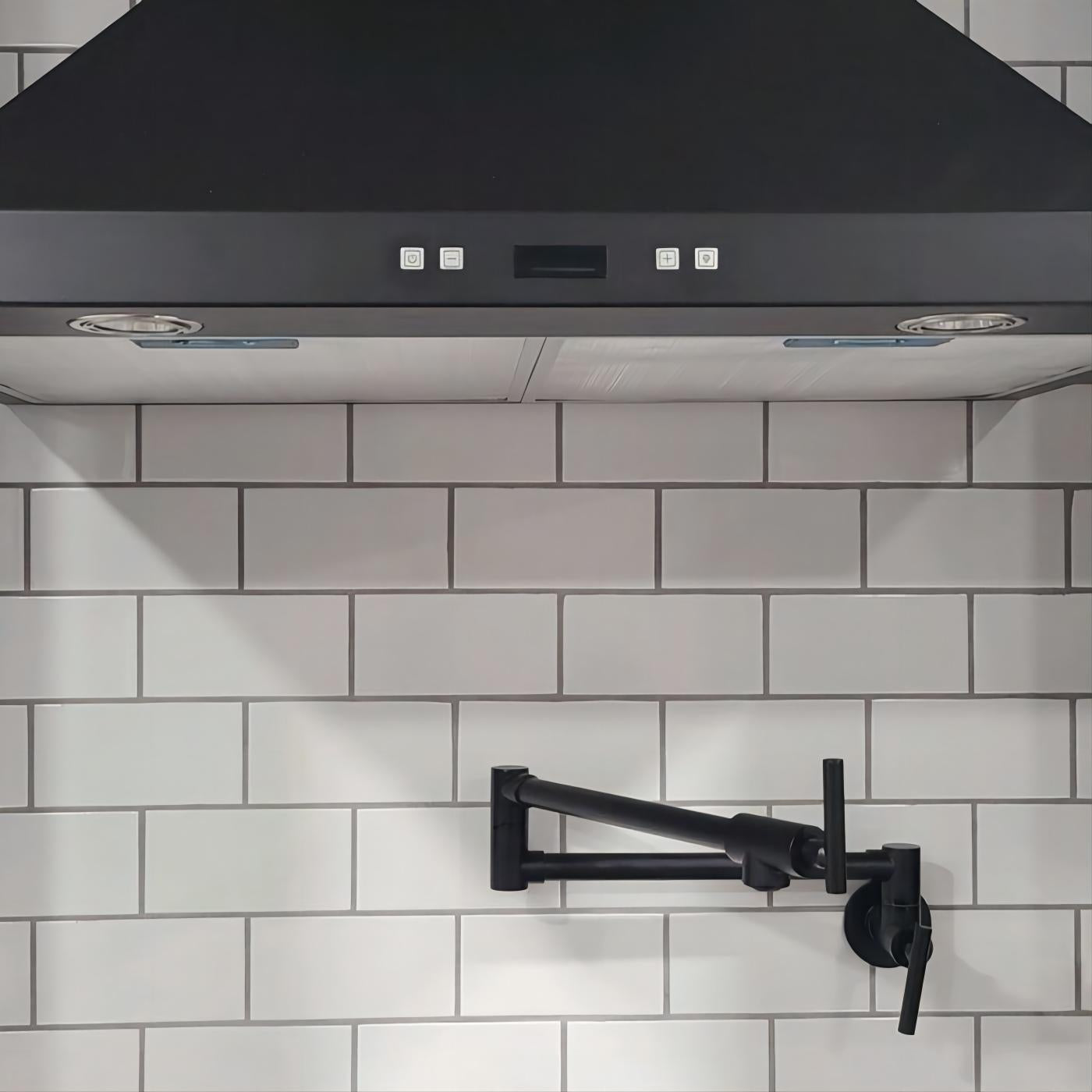 Matte black wall-mount pot filler faucet with swivel brass arm against white subway tiles.