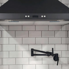 Matte black wall-mount pot filler faucet with swivel brass arm against white subway tiles.