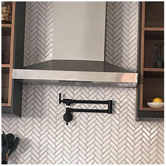 Matte black wall-mount pot filler faucet with swivel brass arm in a kitchen.