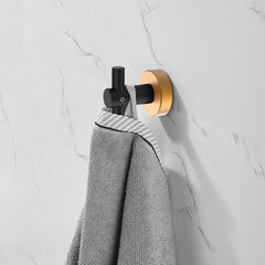 Black gold round base wall hook mounted on white marble wall, holding a gray towel.