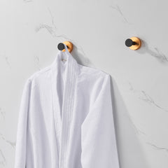 Four black gold round base wall mount towel hooks holding a white robe on a marble wall.