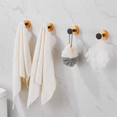 Four black gold round base wall mount towel hooks holding white towels and loofahs on a marble wall.