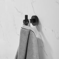 Matte black aluminum wall hook mounted on white marble wall holding a gray towel.