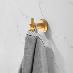 Brushed gold wall mount hook holding a gray towel on white marble wall.