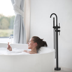 Matte black floor mount bathtub faucet with handheld shower next to a woman in a tub.