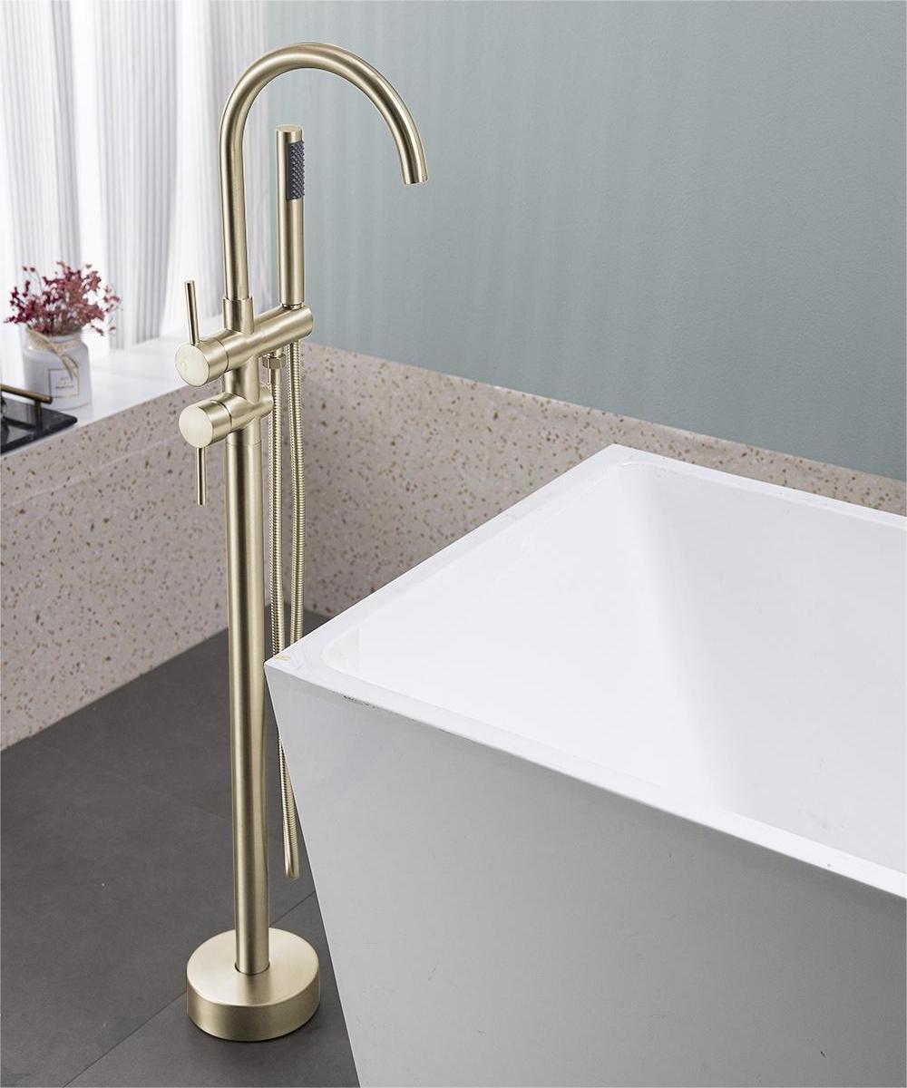 Brushed gold freestanding floor-mount bathtub faucet with curved spout next to white tub.