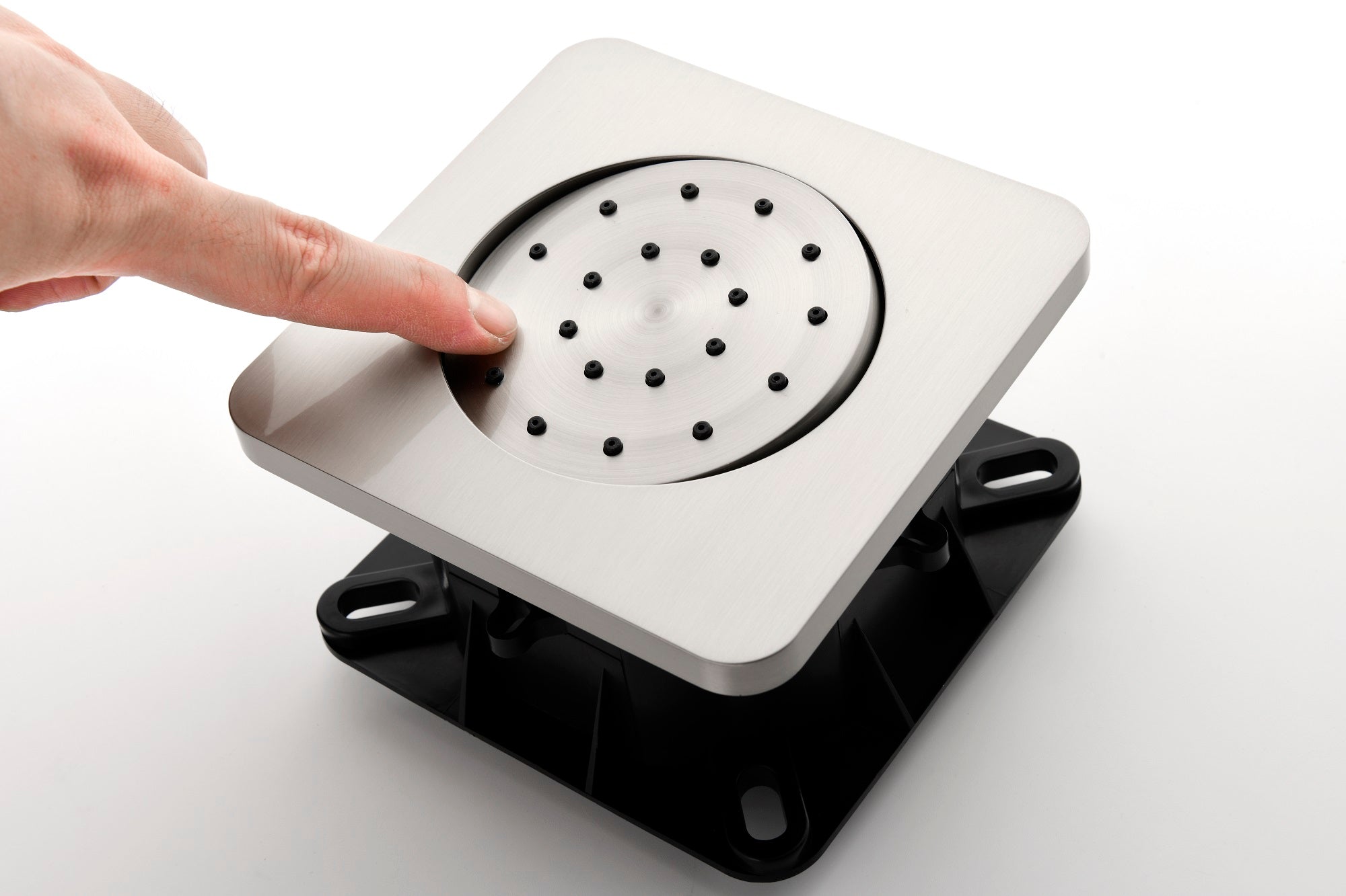 Silver square shower valve with circular perforated center, black base, and hand touching it.