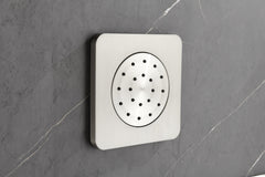 Square chrome showerhead with multiple perforations mounted on gray tiled wall.