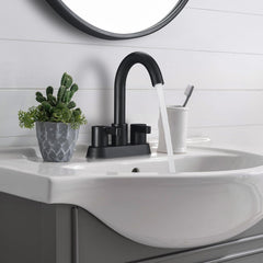 Matte black 2-handle centerset bathroom faucet with pop-up drain mounted on white sink, water flowing from arc spout.