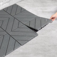Gray interlocking plastic deck tiles being assembled on a floor by hand.