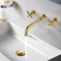 Brushed gold wall-mounted bathroom faucet with cross handles over white sink.