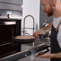 Man holding a 10-inch pre-seasoned cast iron skillet with bread over an oven.