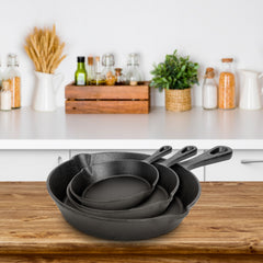 Set of three black cast iron skillets in 6, 8, and 10 inch sizes on a wooden surface.