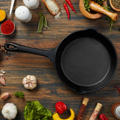 Black cast iron skillet on wooden surface with scattered spices and herbs.