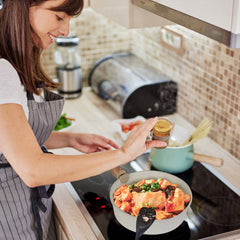 Woman cooking salmon in a white nonstick pan from the Bostome 9-piece cookware set on a kitchen stove.