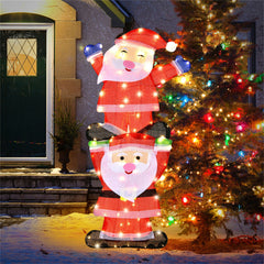 LED-lit inflatable Santa figures stacked on a snowy yard beside a lit Christmas tree.