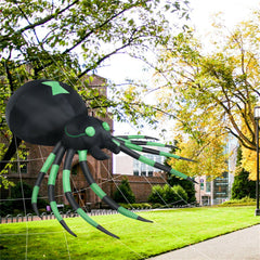 A large black and green inflatable spider with a green arrow on its back is in a park.