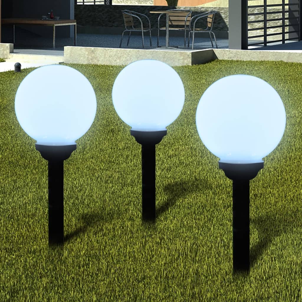 Three white glossy ball solar pathway lights illuminate a green lawn.