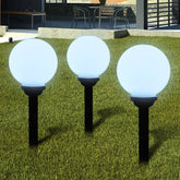 Three white glossy ball solar pathway lights illuminate a green lawn.