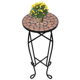 Round terracotta mosaic side table with black iron frame, topped with yellow flowering plant.