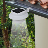 White solar LED light clipped to a gutter, emitting a downward beam in a garden setting.