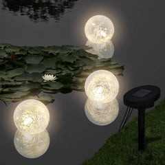 Six glowing white LED solar ball lights floating on a pond with lily pads and a ground spike.
