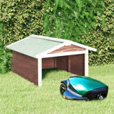 A mocha and white firwood robotic lawn mower garage with a green mower positioned in front on grass.