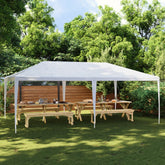 White 13.1'x19.7' party tent with UV water-resistant canopy set up in a green backyard with wooden picnic tables.