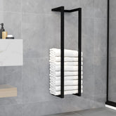 Black iron towel rack with four rungs holding stacked white towels on a gray bathroom wall.