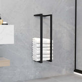 Black iron towel rack mounted on gray tiled wall holding stacked white towels.