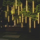 20 pieces of 2ft warm white meteor rain lights with 720 LEDs cascading from a tree at night.