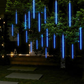 Blue LED meteor shower string lights hanging from tree branches outdoors at night.