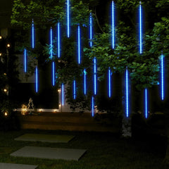 Blue LED meteor shower string lights hanging from tree branches outdoors at night.