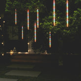 Eight 2-foot colorful LED meteor rain lights hanging from a tree at night, creating a cascading rainbow shower effect.