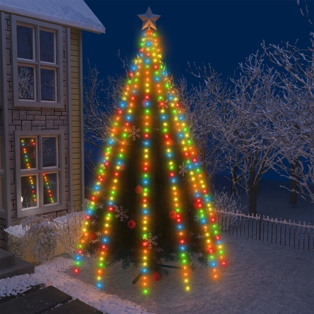 A tall Christmas tree wrapped in colorful 500 LED string lights with star topper, set outdoors near a house at night.