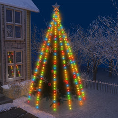 A tall Christmas tree wrapped in colorful 500 LED string lights with star topper, set outdoors near a house at night.