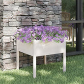 White solid pine cube garden planter with purple flowers against a stone wall.
