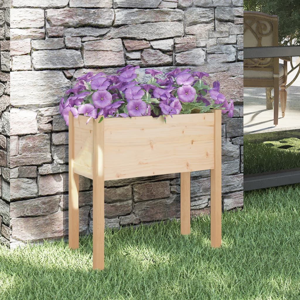 Wooden pine garden planter with purple petunias, against stone wall on grass.