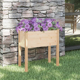 Wooden pine garden planter with purple petunias, against stone wall on grass.