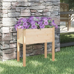 Wooden pine garden planter with purple petunias, against stone wall on grass.