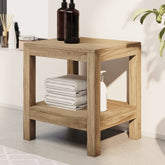Solid teak wood bathroom side table with lower shelf holding folded towels and a lotion bottle.