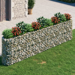Galvanized iron gabion raised bed filled with rocks and red flowers in a garden setting.