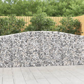 Arched galvanized gabion baskets forming a curved stone wall against a wooden patio.