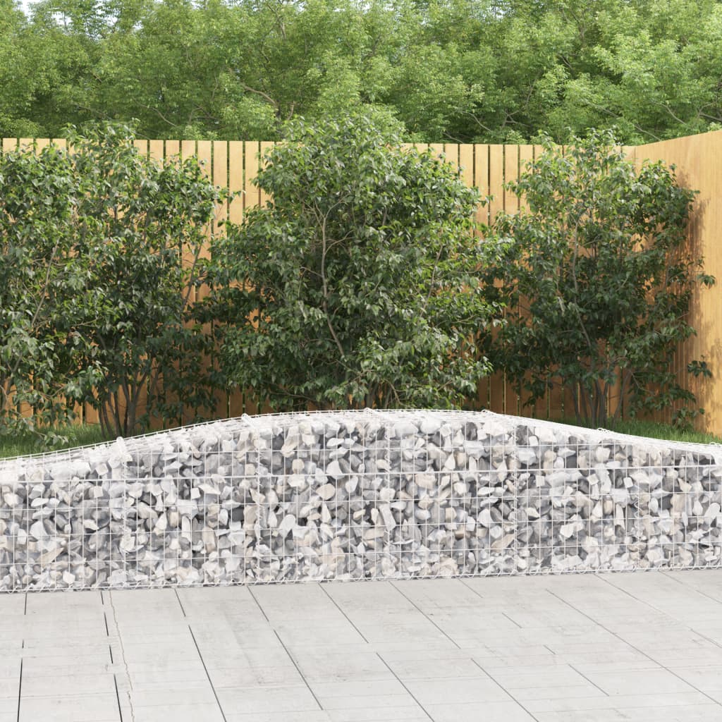 Two galvanized arched gabion baskets filled with rocks, forming a curved garden wall beside a wooden fence.