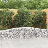 Two galvanized arched gabion baskets filled with rocks, forming a curved garden wall beside a wooden fence.