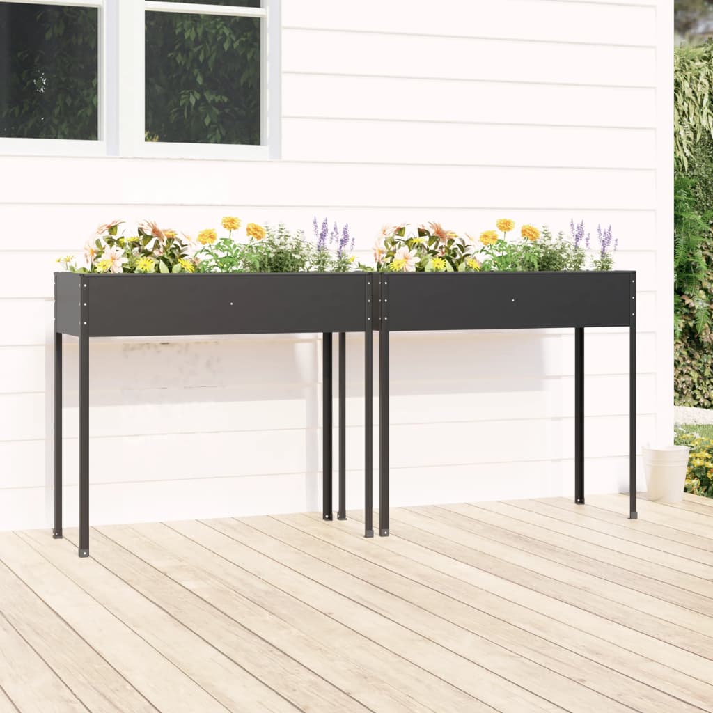 Two anthracite galvanized steel garden planters with flowers, on a wooden deck against a white house.