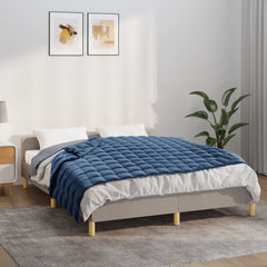 A blue weighted blanket with quilted squares on a gray bed in a bright room.